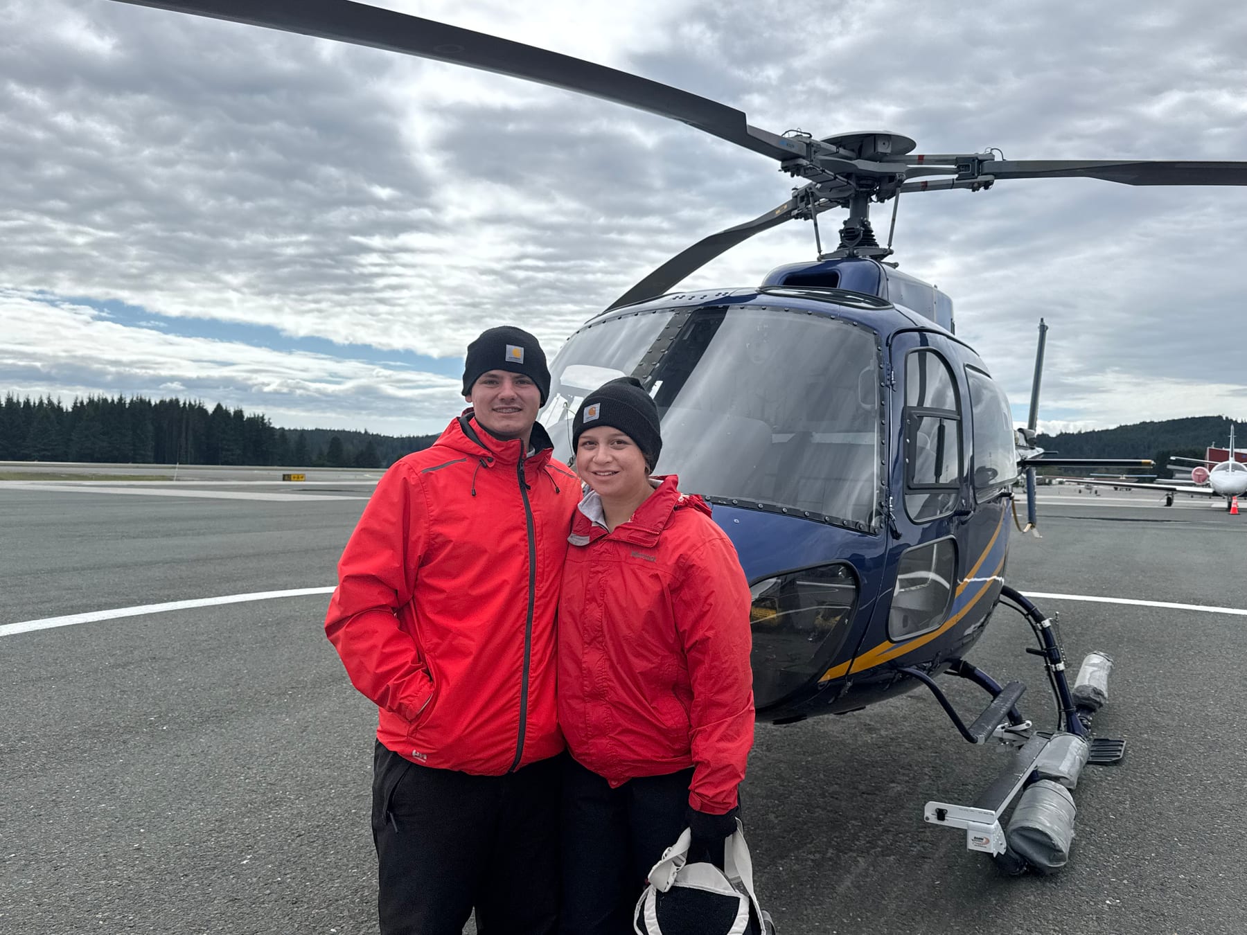 Tyler Cardwell and Heather standing in front of a helicopter in Alaska