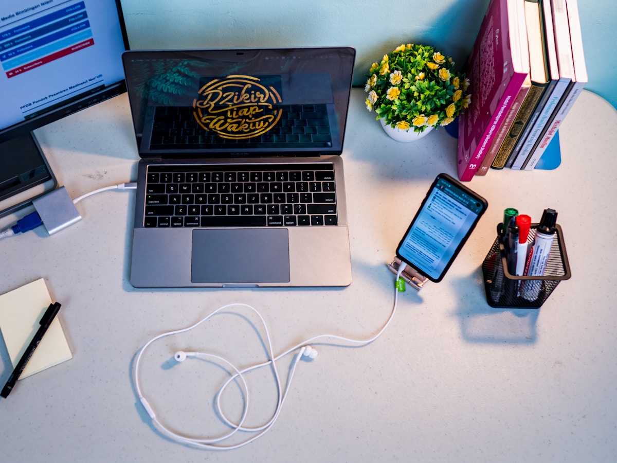 Laptop and smartphone on a desk with books and office supplies.