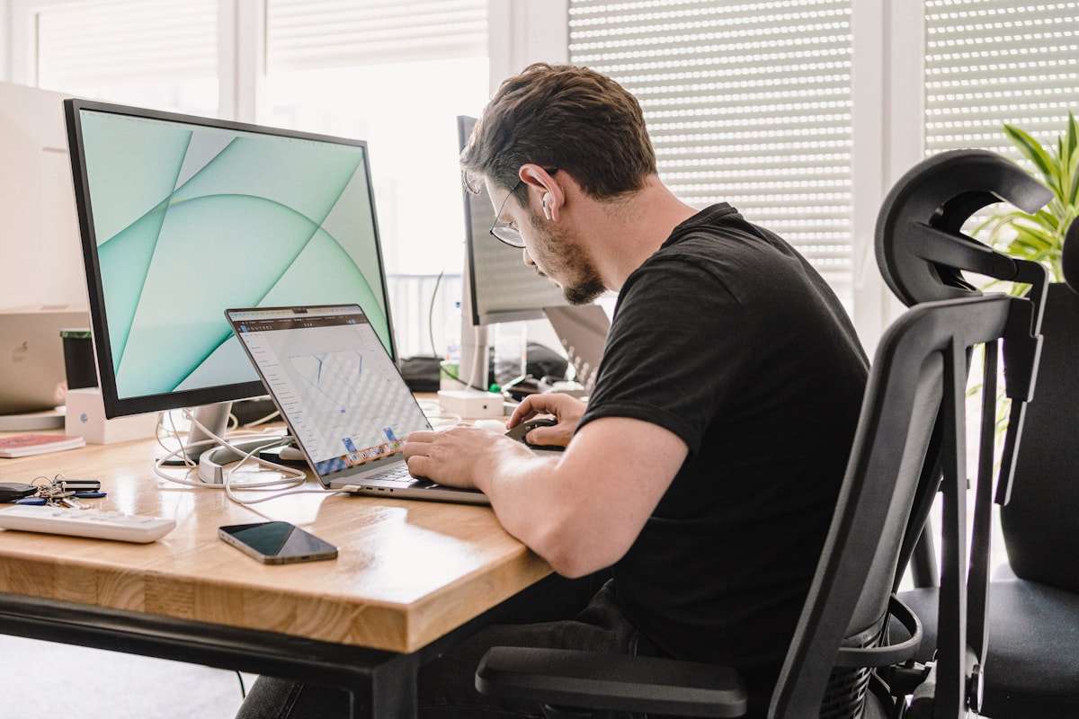 Web designer working at a desk with a monitor and laptop